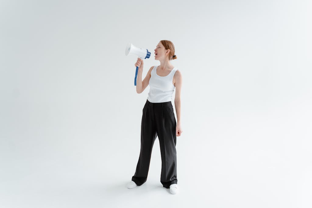 Woman in casual attire speaking through a megaphone in a bright studio setting.