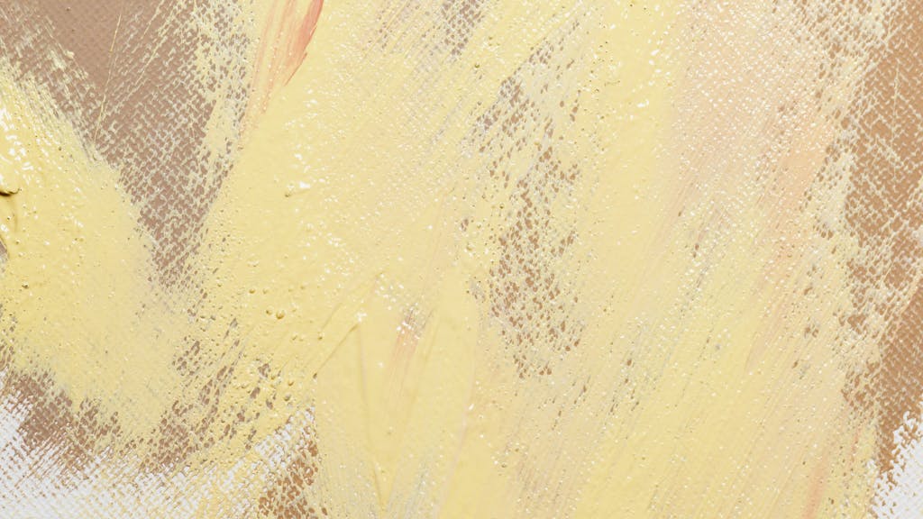 A close-up of an abstract painting with yellow and beige textured strokes on canvas.