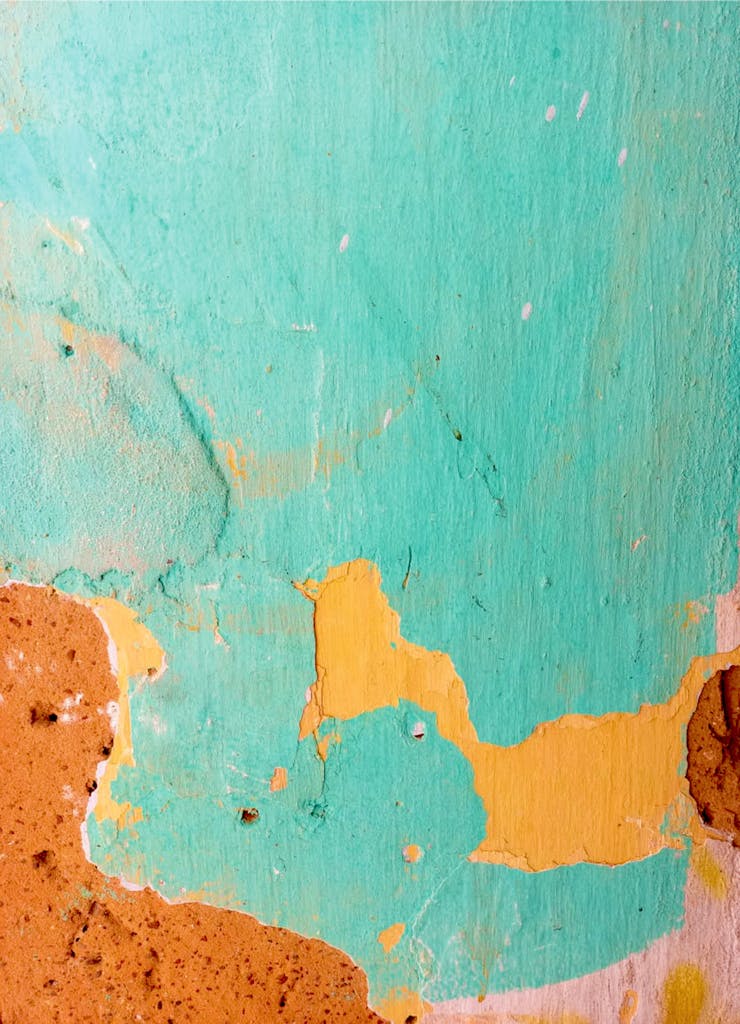 Artistic close-up of a textured wall with peeling turquoise and ochre paint, ideal for abstract backgrounds.